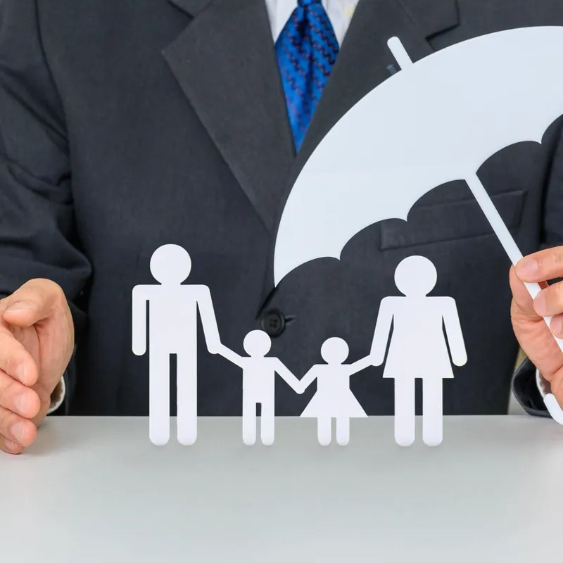 Hands sheltering a paper family under an umbrella